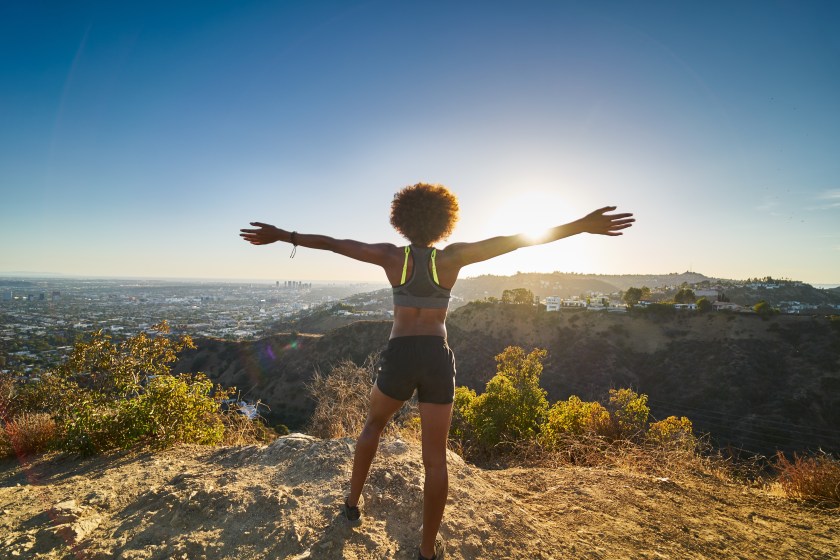 athletic african american woman celebrating reaching top of runyon canyon with arms open